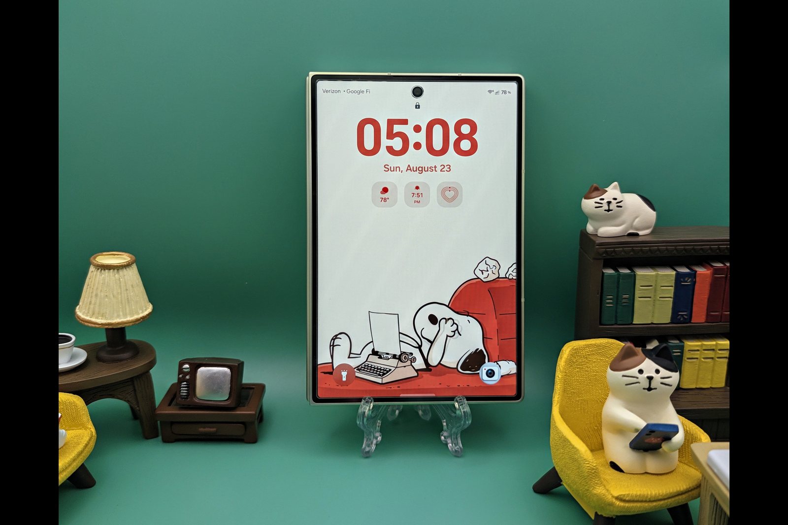 Galaxy Z Fold 8 closed, standing on a clear stand against a teal background, showing its lock screen