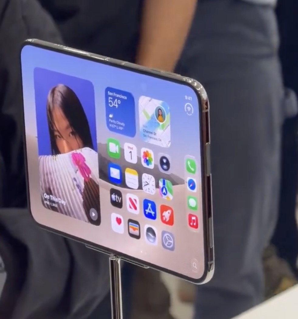 The iPhone Duo open on a metal stand in the hands on area, showing a home screen with a Photos memory and a live Maps card
